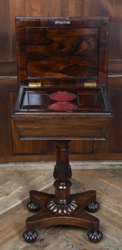 A Victorian dark rosewood teapoy featuring a sarcophagus-shaped chest top resting on a turned carved pedestal and quadruped base. View V