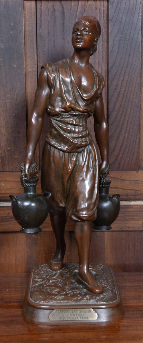 A dark brown patinated bronze sculpture depicting a standing Tunisian water bearer carrying two vessels on a rectangular moulded base. View V