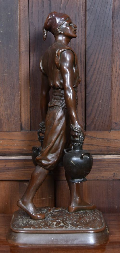 A dark brown patinated bronze sculpture depicting a standing Tunisian water bearer carrying two vessels on a rectangular moulded base. View VI