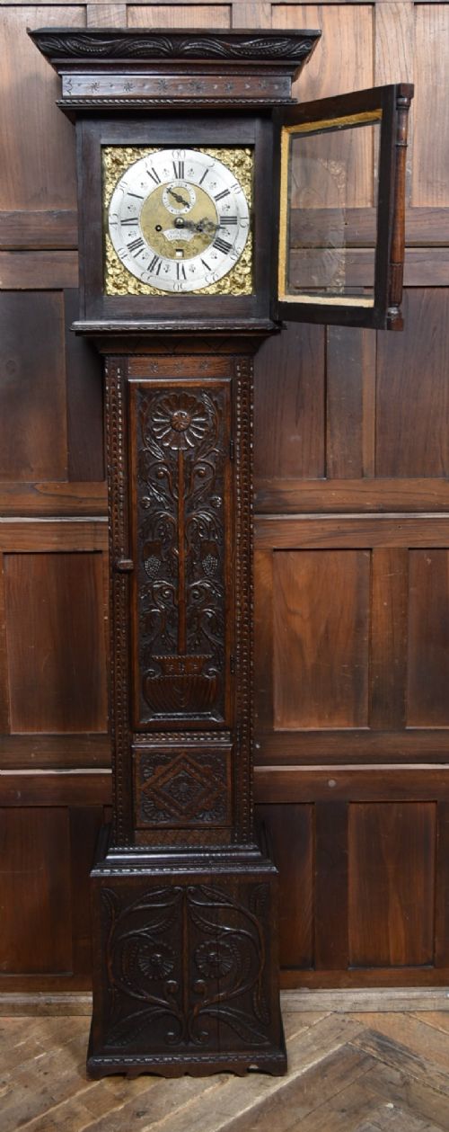 fig 1. A tall carved dark oak longcase grandfather clock featuring intricate carved floral panels on the trunk and a brass dial signed John Smith Macclesfield.