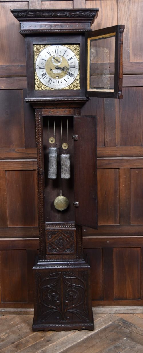 A tall carved dark oak longcase grandfather clock featuring intricate carved floral panels on the trunk and a brass dial signed John Smith Macclesfield. View VII