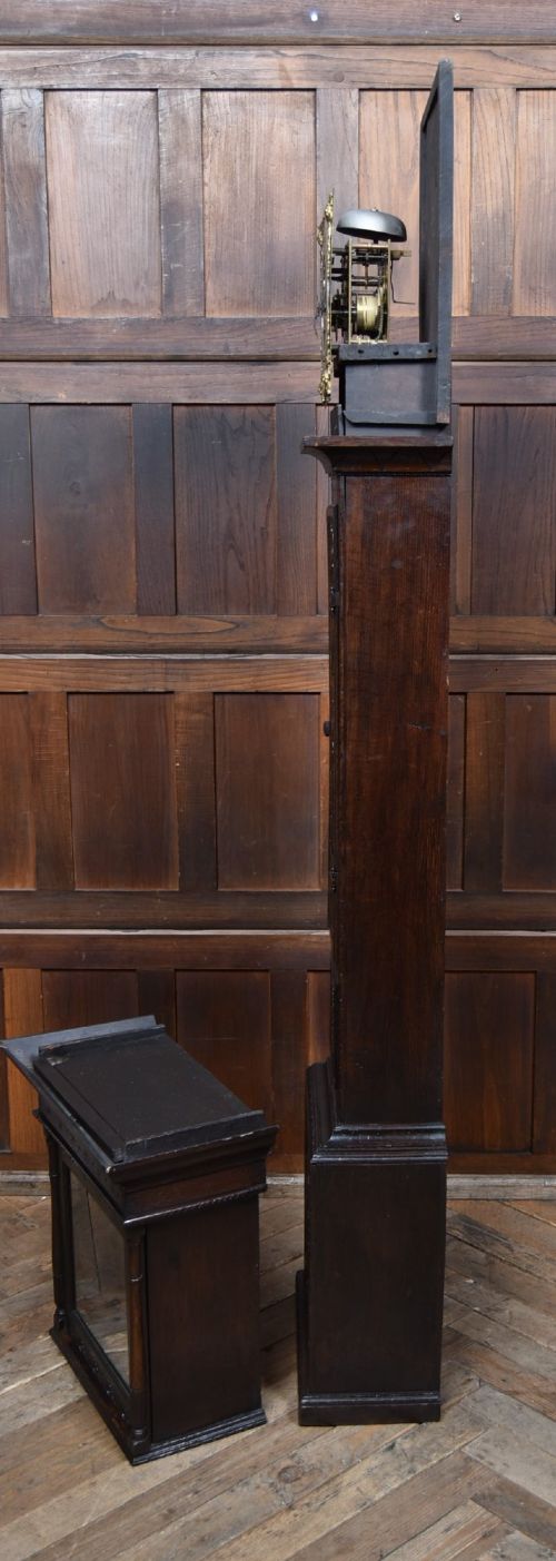 A tall carved dark oak longcase grandfather clock featuring intricate carved floral panels on the trunk and a brass dial signed John Smith Macclesfield. View XI