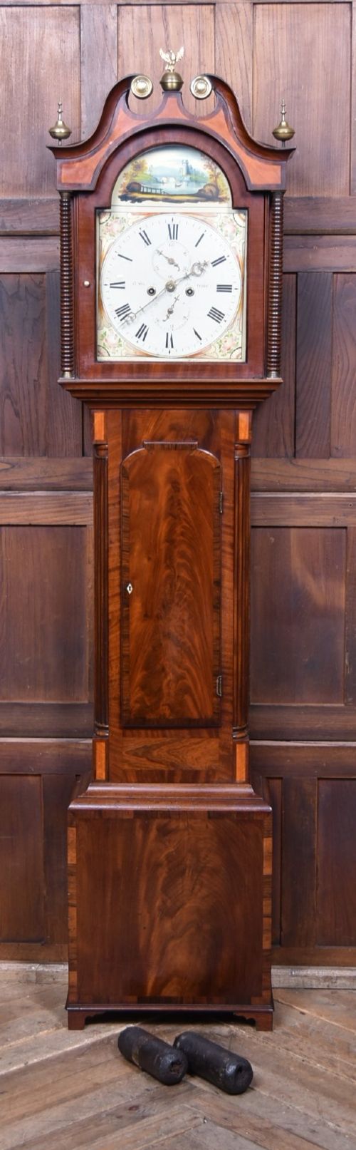 fig 1. An antique Scottish flame mahogany longcase clock featuring a swan-neck pediment with brass finials and an arched painted dial.