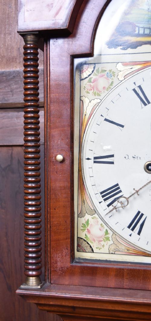 An antique Scottish flame mahogany longcase clock featuring a swan-neck pediment with brass finials and an arched painted dial. View III