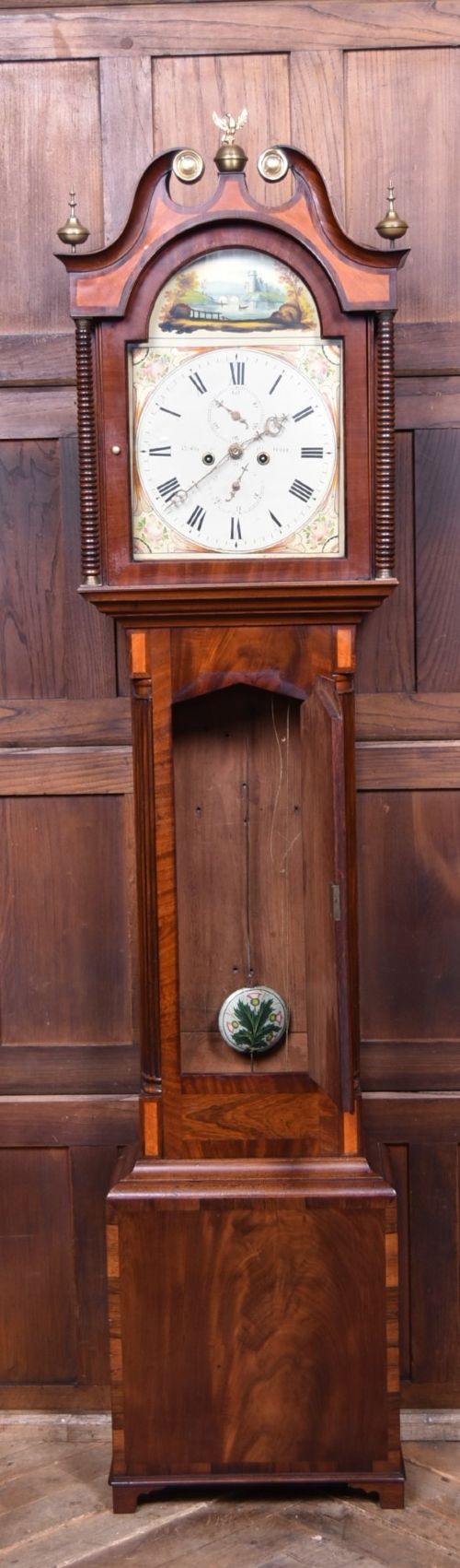 An antique Scottish flame mahogany longcase clock featuring a swan-neck pediment with brass finials and an arched painted dial. View IX