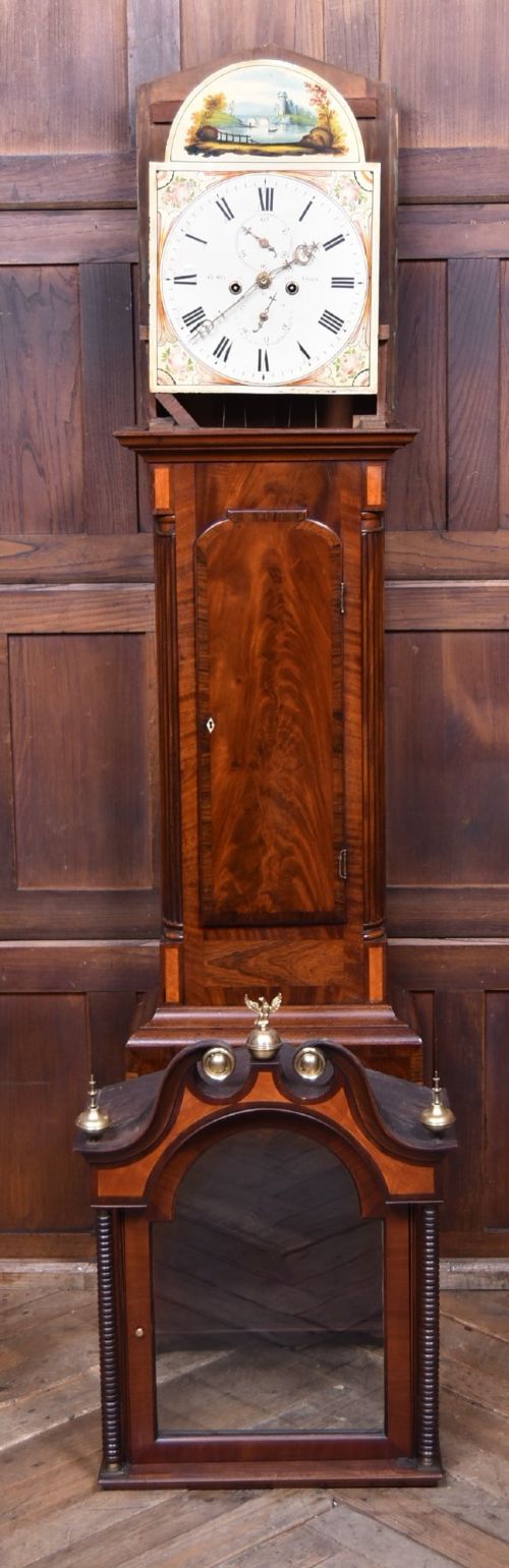 An antique Scottish flame mahogany longcase clock featuring a swan-neck pediment with brass finials and an arched painted dial. View X