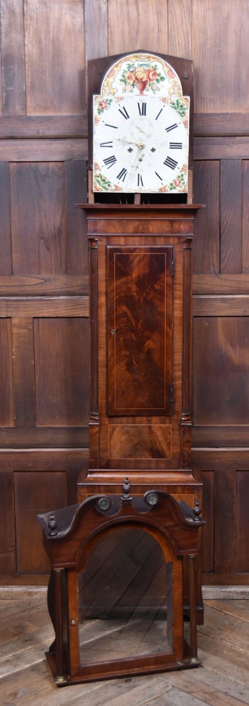 A Scottish mahogany longcase clock featuring a swan-neck pediment with brass finials, a hand-painted dial face, and flame mahogany veneers. View X