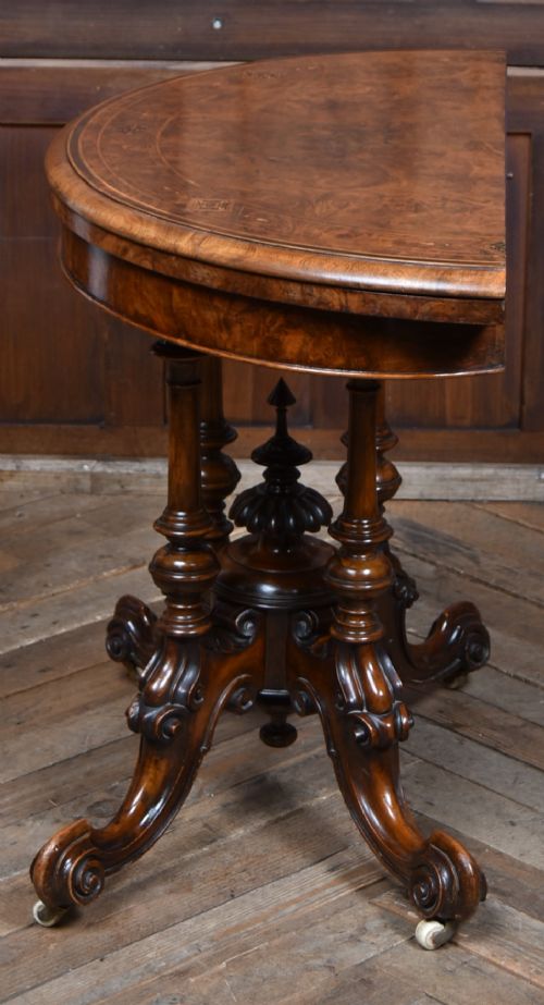 A Victorian burr walnut fold-over games table featuring a semi-circular top, dual turned column pedestal base, carved scroll legs, and ceramic castors. View XII