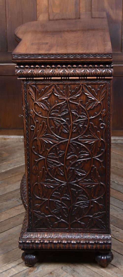 A nineteenth-century padouk wood sideboard featuring high-relief foliate hand-carving across four panelled cupboard doors and a breakfront profile. View XV