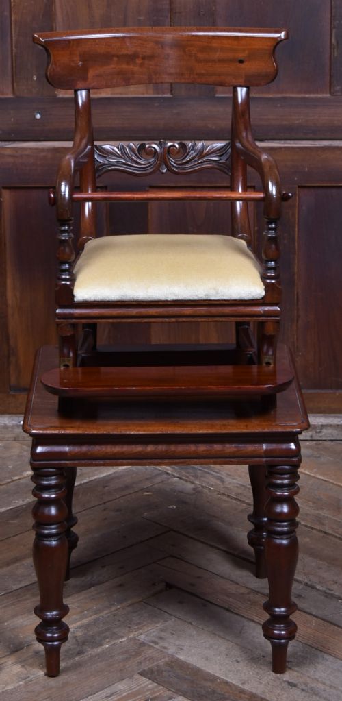 A Victorian metamorphic mahogany childs high chair with turned legs, curved armrests, a carved backrest crest, and cream fabric upholstery. View II