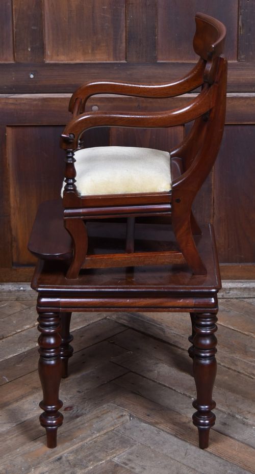A Victorian metamorphic mahogany childs high chair with turned legs, curved armrests, a carved backrest crest, and cream fabric upholstery. View VII