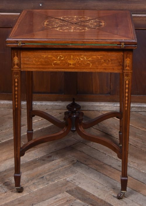 An Edwardian mahogany envelope card table featuring satinwood marquetry inlay, a single drawer, and a curved cross-stretcher with brass castors. View XIV