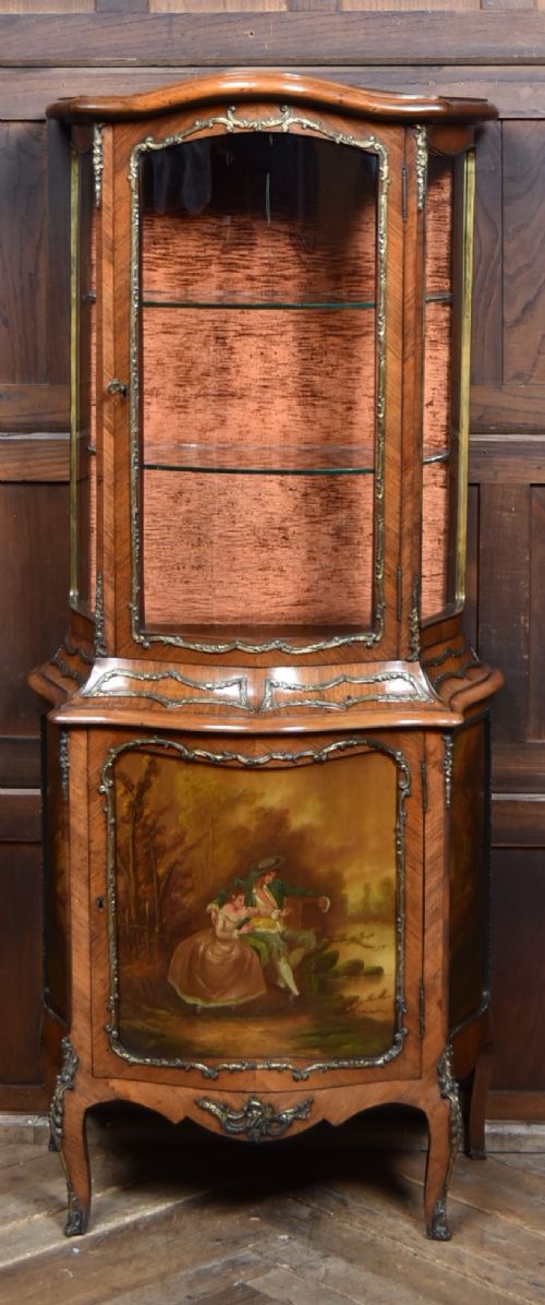 fig 1. A French walnut vitrine cabinet featuring curved glass upper panels, gilt-bronze ormolu mounts, cabriole legs, and a hand-painted lower door panel depicting a figurative scene.