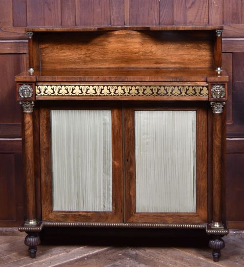 fig 1. A Victorian dark rosewood chiffonier cabinet featuring a decorative brass inlay border, brass mask accents, two pleated silk fabric door panels, turned feet, and a raised upper tier shelf.