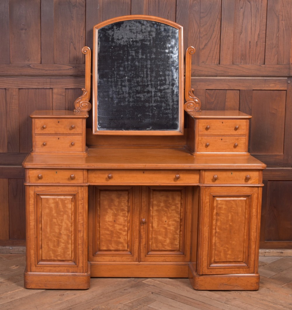 A Victorian satinwood dressing table featuring an arched central swivel mirror, trinket drawers, frieze drawers, and lower pedestal cupboards.