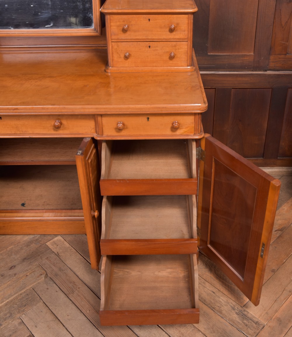 A Victorian satinwood dressing table featuring an arched central swivel mirror, trinket drawers, frieze drawers, and lower pedestal cupboards. View V