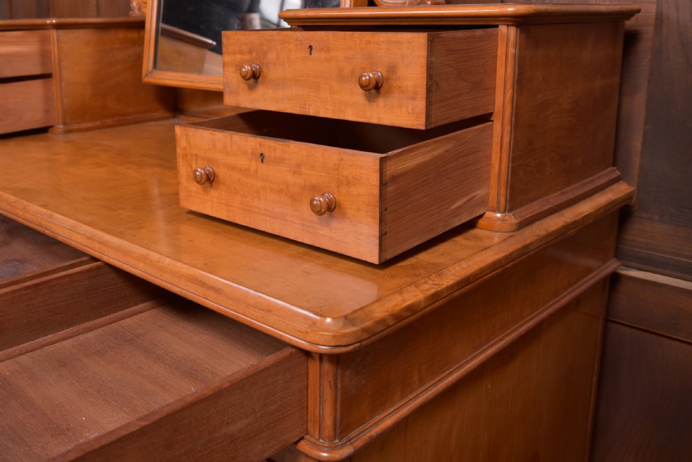 A Victorian satinwood dressing table featuring an arched central swivel mirror, trinket drawers, frieze drawers, and lower pedestal cupboards. View VII