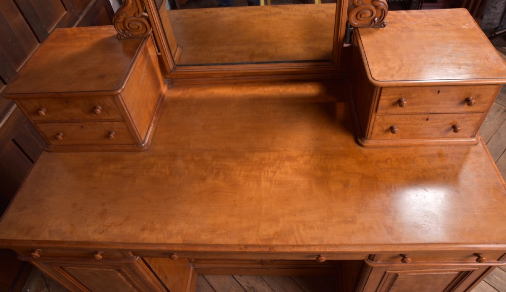 A Victorian satinwood dressing table featuring an arched central swivel mirror, trinket drawers, frieze drawers, and lower pedestal cupboards. View X