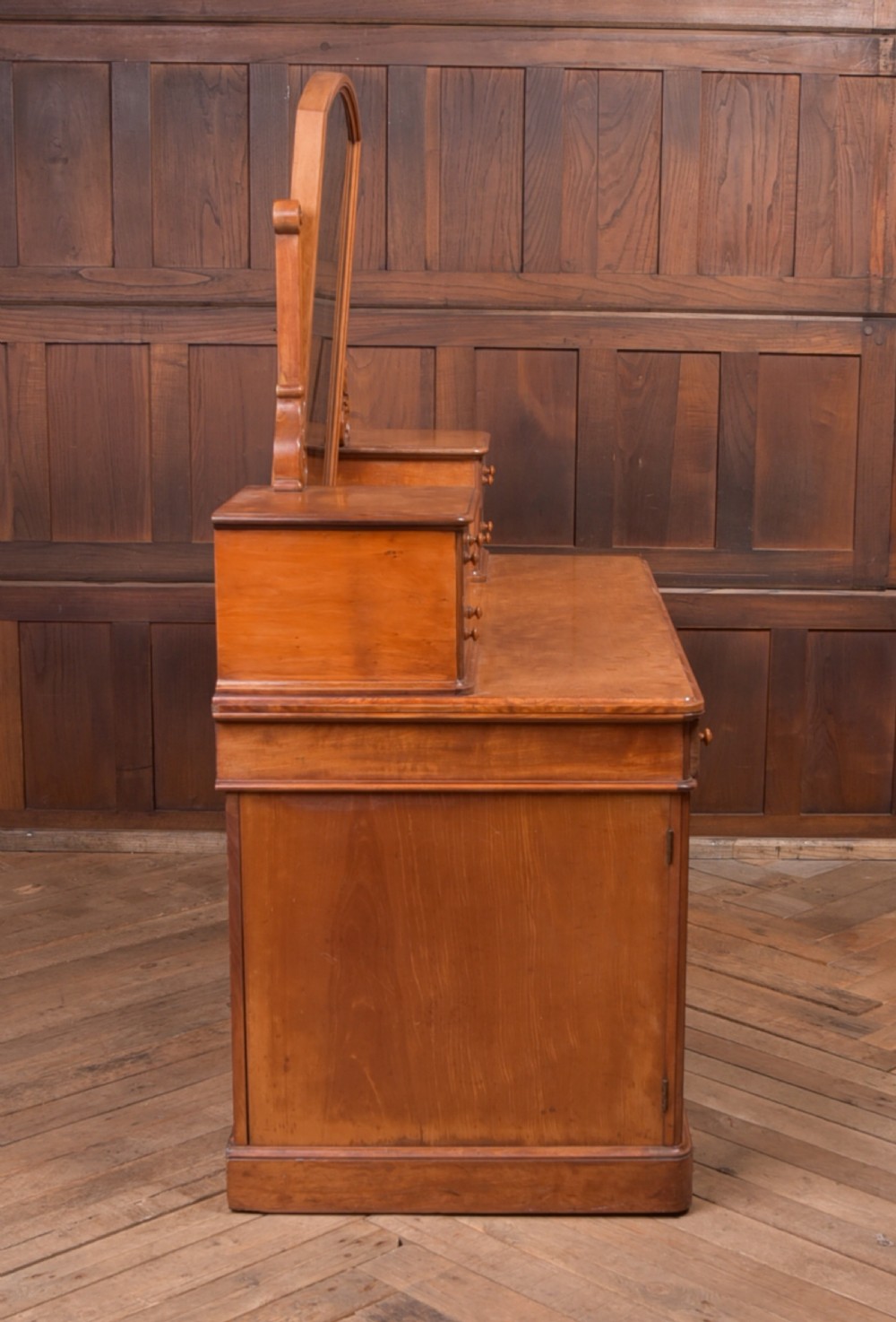 A Victorian satinwood dressing table featuring an arched central swivel mirror, trinket drawers, frieze drawers, and lower pedestal cupboards. View XII