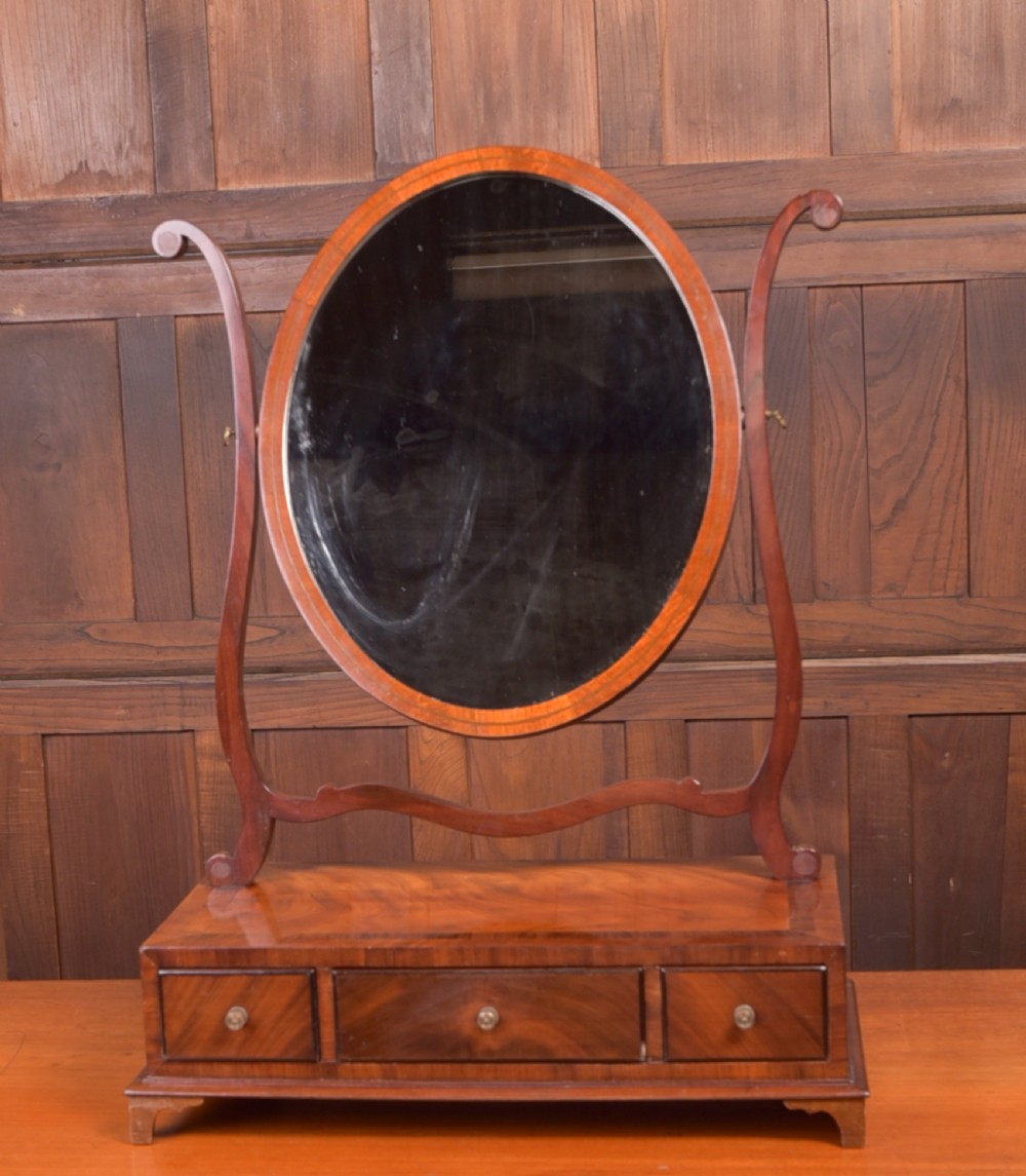 An antique mahogany oval toilet mirror with curved horn supports atop a plinth base containing three small drawers.