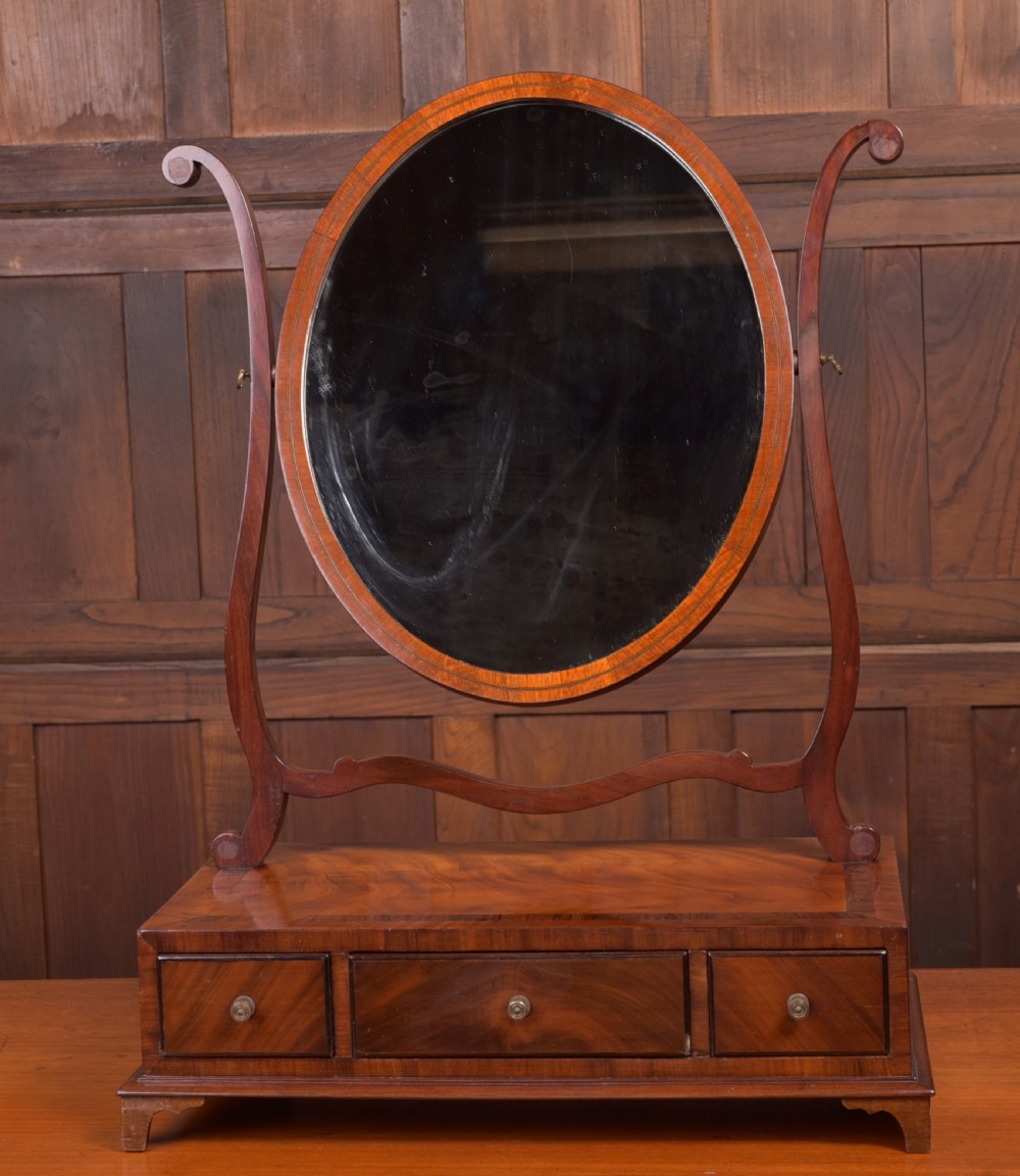 An antique mahogany oval toilet mirror with curved horn supports atop a plinth base containing three small drawers. View III