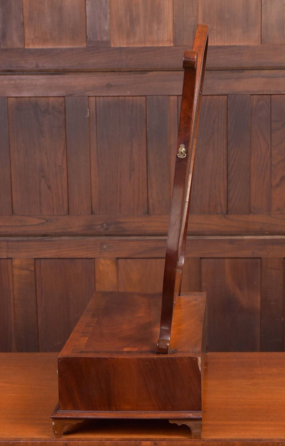 An antique mahogany oval toilet mirror with curved horn supports atop a plinth base containing three small drawers. View IV
