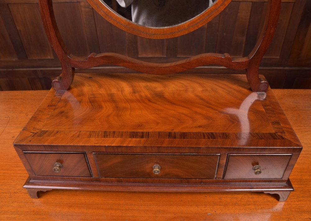 An antique mahogany oval toilet mirror with curved horn supports atop a plinth base containing three small drawers. View V
