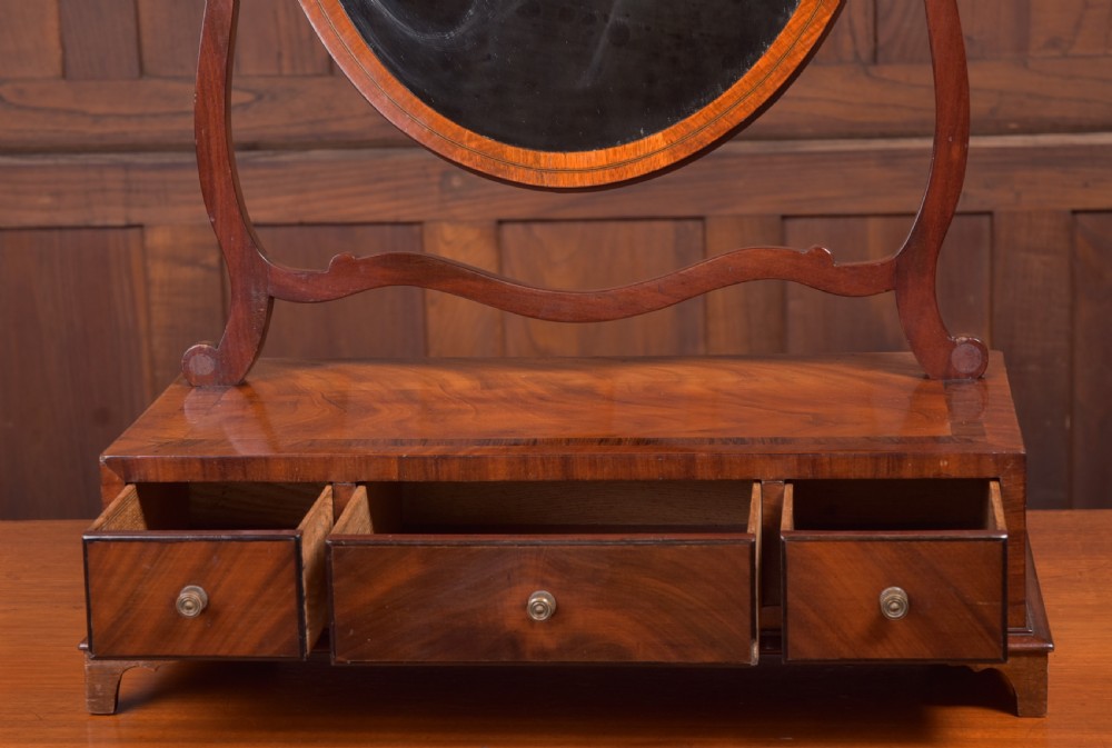 An antique mahogany oval toilet mirror with curved horn supports atop a plinth base containing three small drawers. View VI