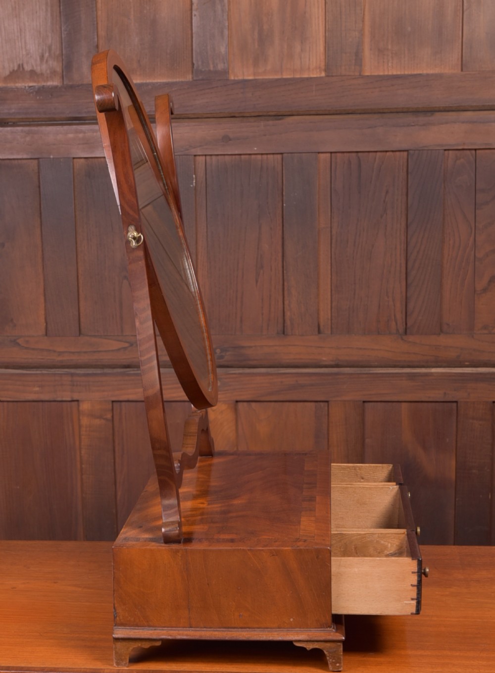 An antique mahogany oval toilet mirror with curved horn supports atop a plinth base containing three small drawers. View VII