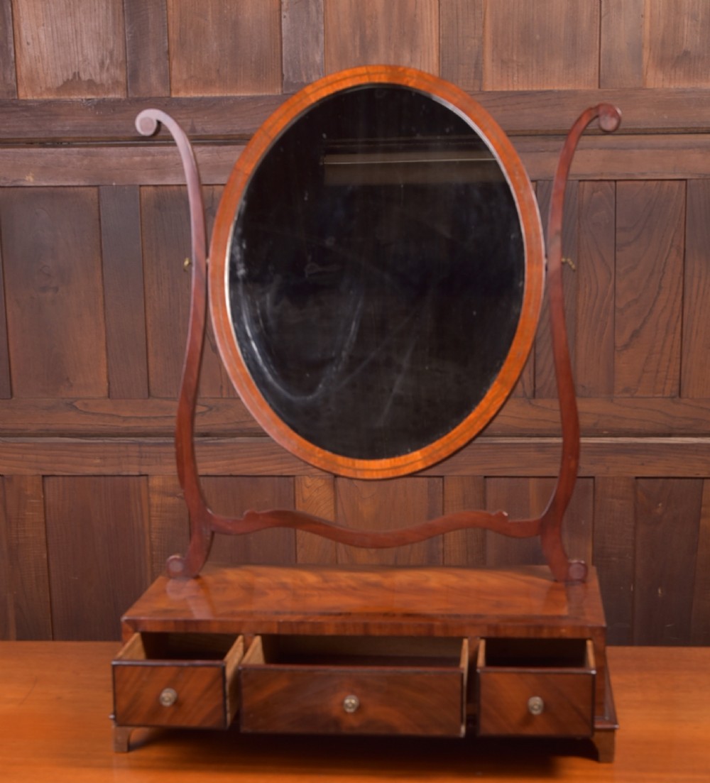 An antique mahogany oval toilet mirror with curved horn supports atop a plinth base containing three small drawers. View VIII