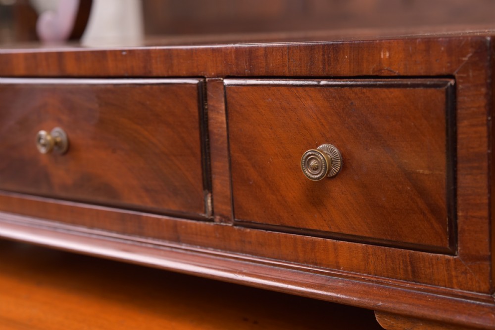 An antique mahogany oval toilet mirror with curved horn supports atop a plinth base containing three small drawers. View XII