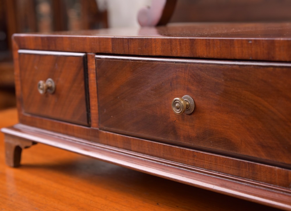 An antique mahogany oval toilet mirror with curved horn supports atop a plinth base containing three small drawers. View XIV