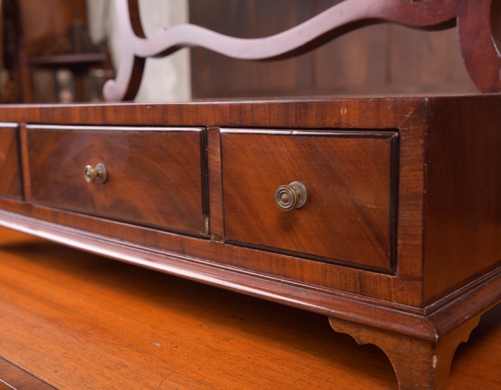 An antique mahogany oval toilet mirror with curved horn supports atop a plinth base containing three small drawers. View XV