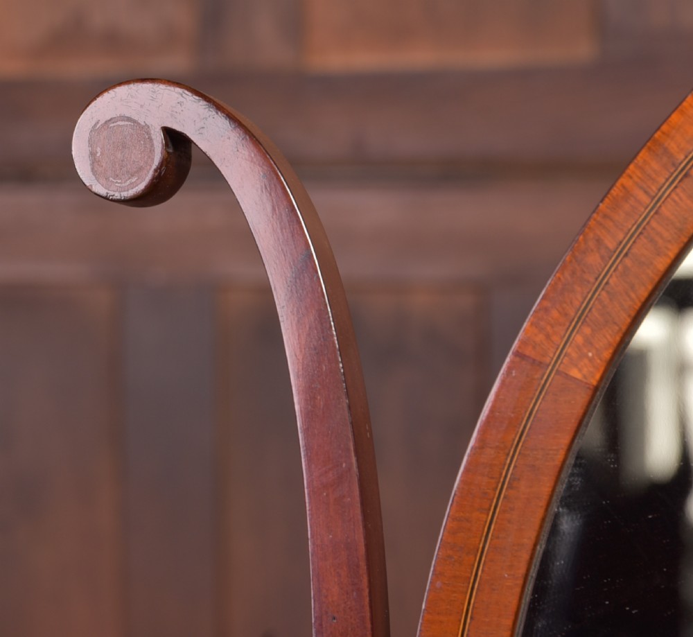 An antique mahogany oval toilet mirror with curved horn supports atop a plinth base containing three small drawers. View XVII