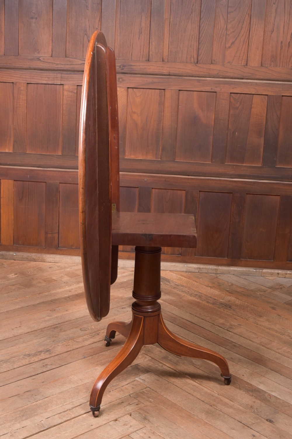 An antique Regency mahogany snap top table with a round crossbanded top, central turned pedestal, four splayed sabre legs, and brass castors. View IV