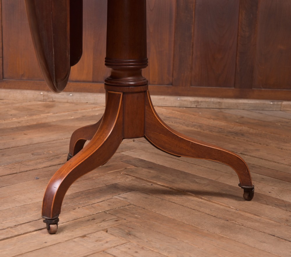 An antique Regency mahogany snap top table with a round crossbanded top, central turned pedestal, four splayed sabre legs, and brass castors. View V