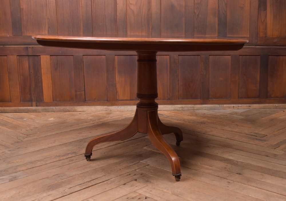 An antique Regency mahogany snap top table with a round crossbanded top, central turned pedestal, four splayed sabre legs, and brass castors. View VI
