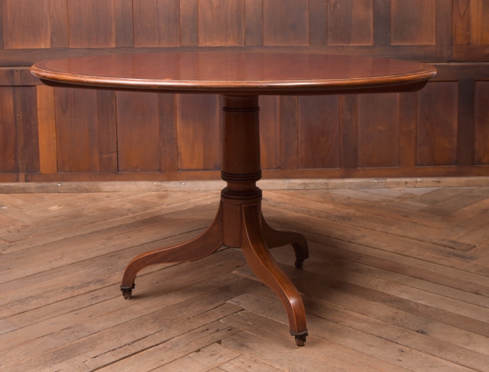 An antique Regency mahogany snap top table with a round crossbanded top, central turned pedestal, four splayed sabre legs, and brass castors. View VII