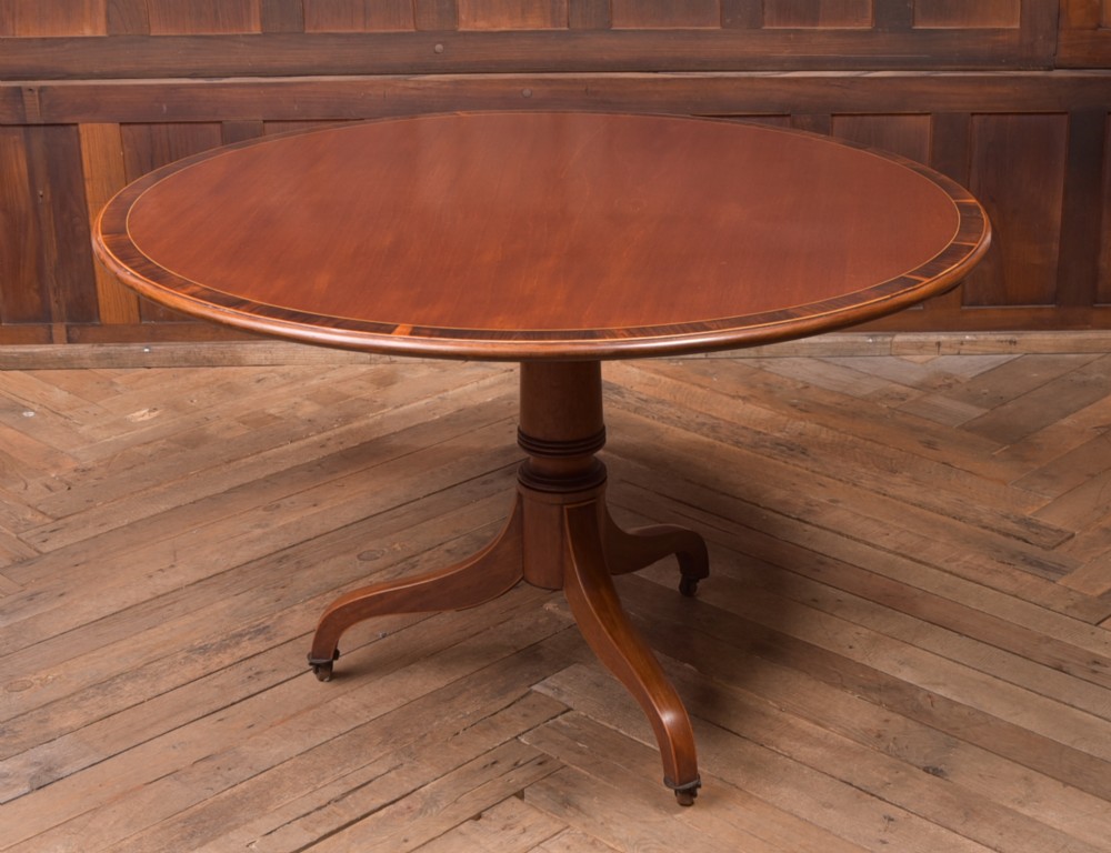 An antique Regency mahogany snap top table with a round crossbanded top, central turned pedestal, four splayed sabre legs, and brass castors. View VIII