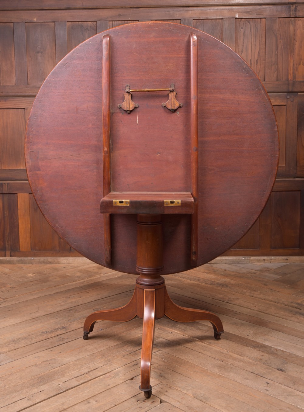 An antique Regency mahogany snap top table with a round crossbanded top, central turned pedestal, four splayed sabre legs, and brass castors. View IX