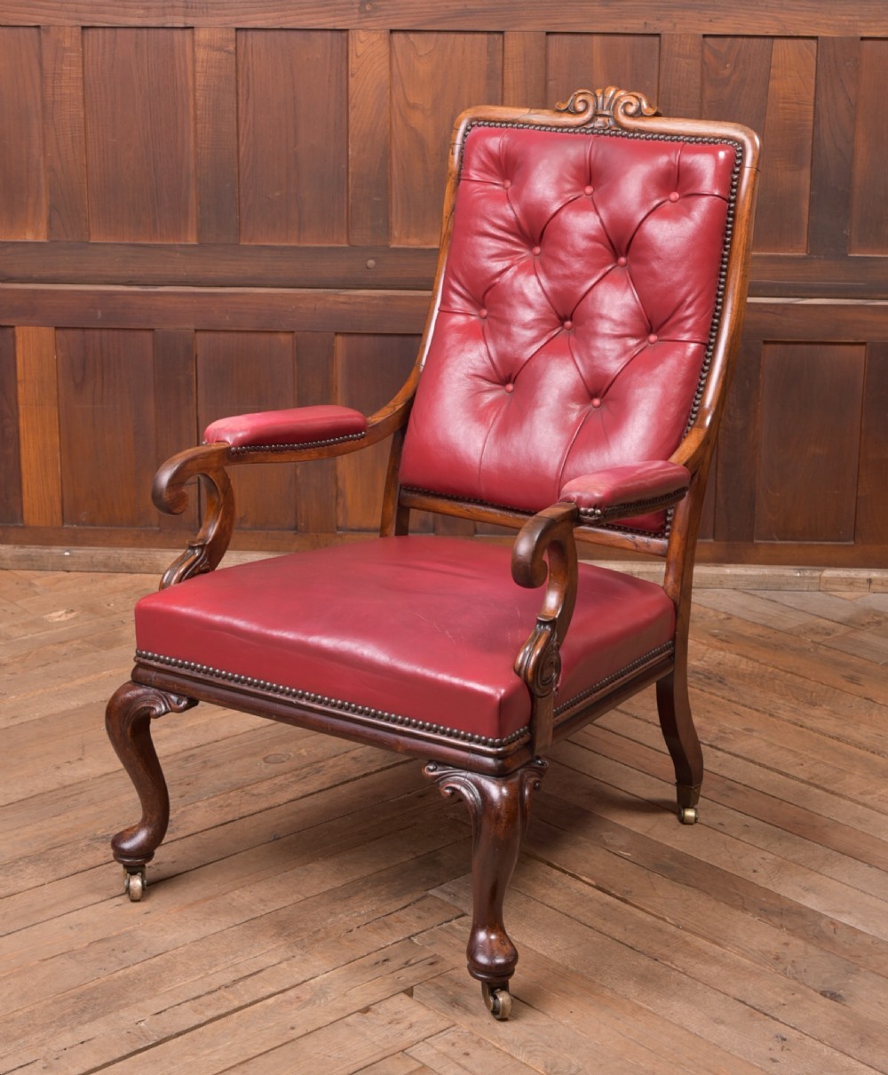 A Regency period rosewood armchair featuring dark red button-tufted leather upholstery, scrolled armrests, brass castors, and carved timber detailing.