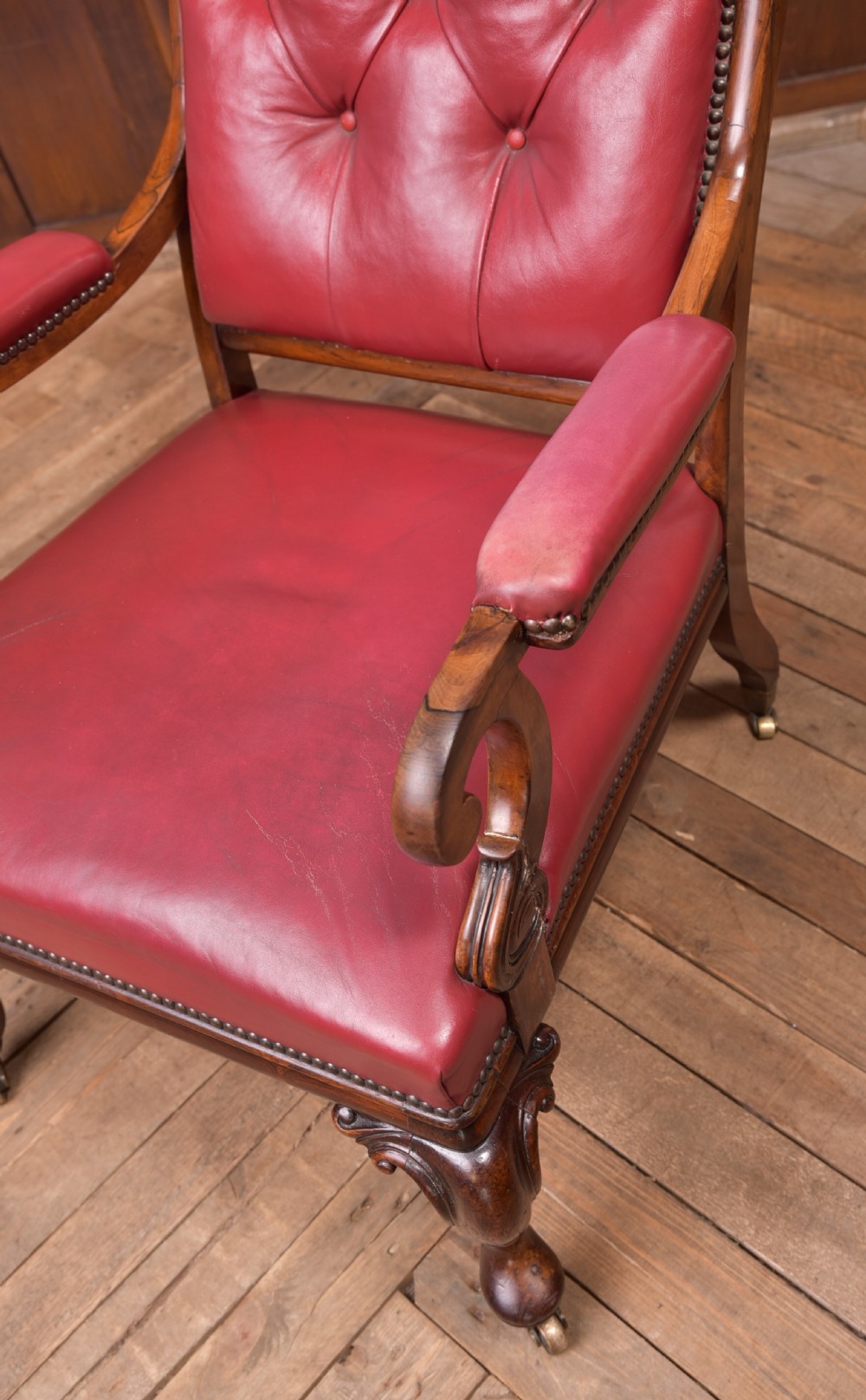 A Regency period rosewood armchair featuring dark red button-tufted leather upholstery, scrolled armrests, brass castors, and carved timber detailing. View III