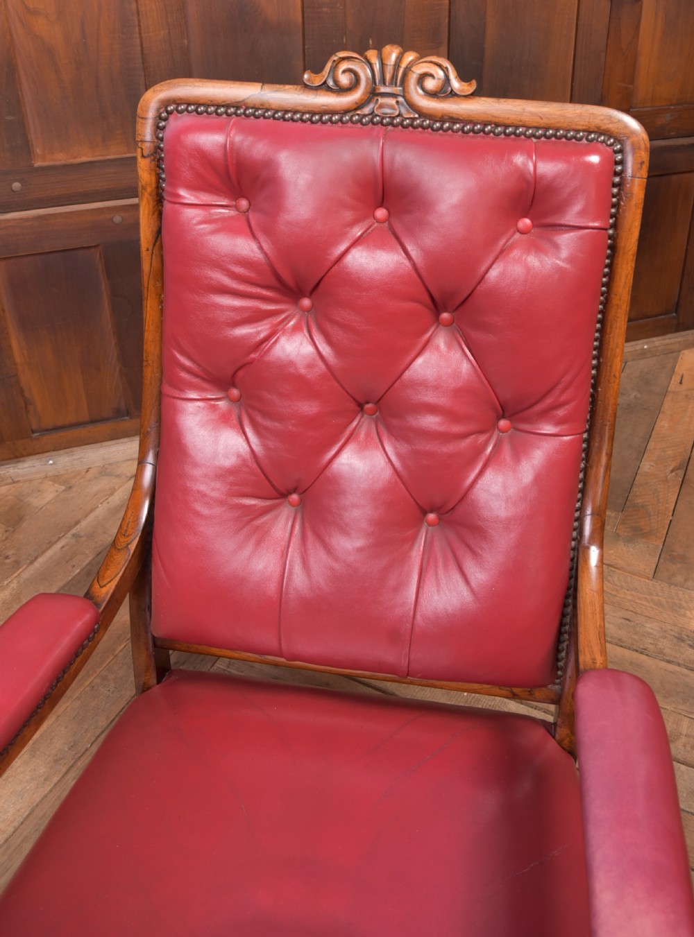 A Regency period rosewood armchair featuring dark red button-tufted leather upholstery, scrolled armrests, brass castors, and carved timber detailing. View V