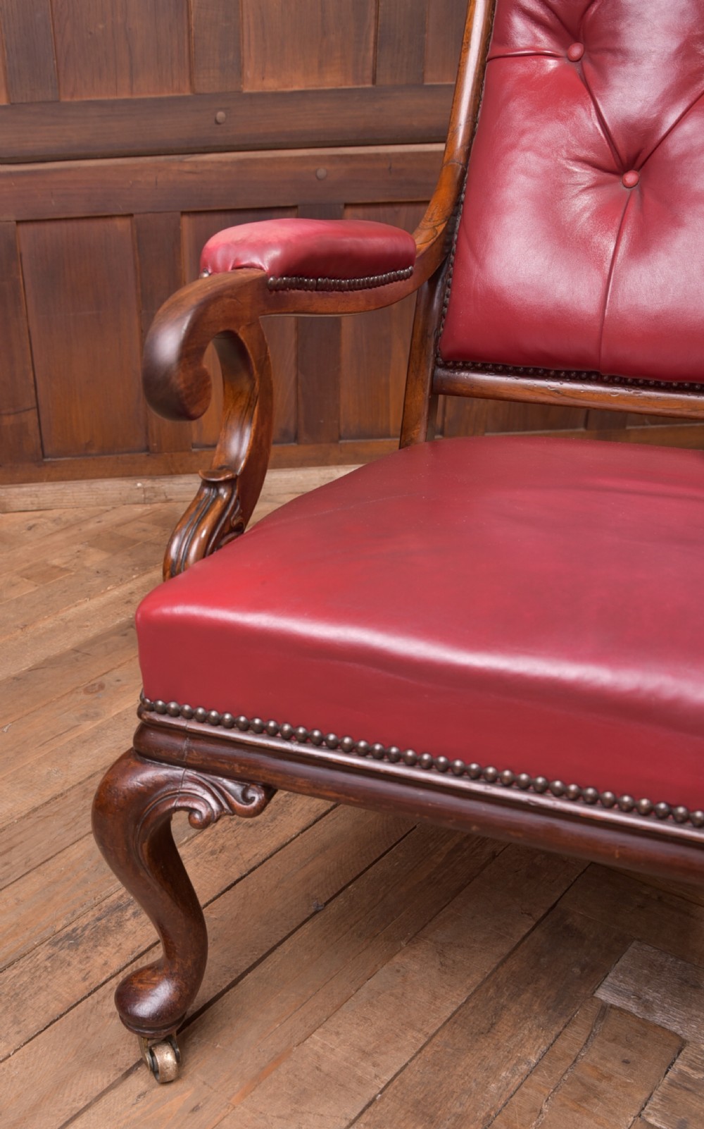 A Regency period rosewood armchair featuring dark red button-tufted leather upholstery, scrolled armrests, brass castors, and carved timber detailing. View VI