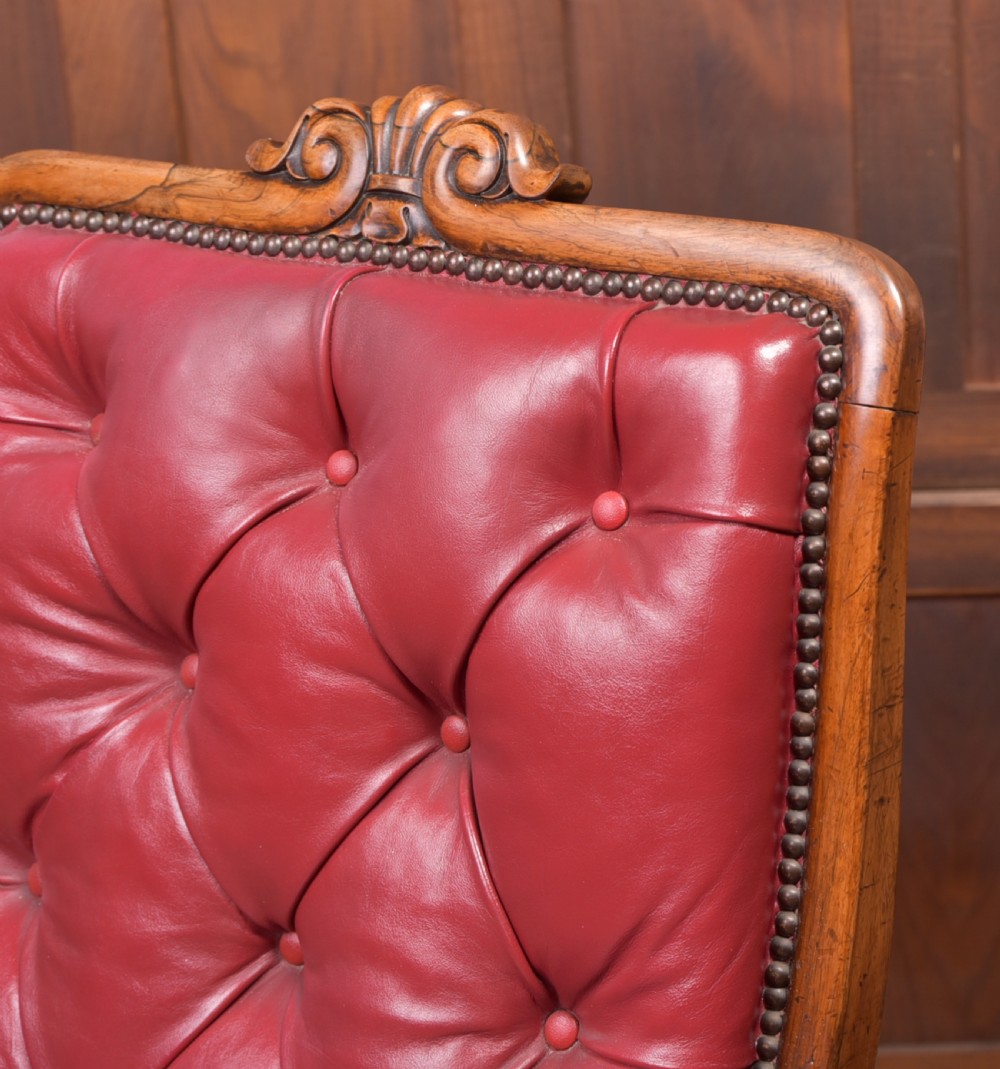 A Regency period rosewood armchair featuring dark red button-tufted leather upholstery, scrolled armrests, brass castors, and carved timber detailing. View VII