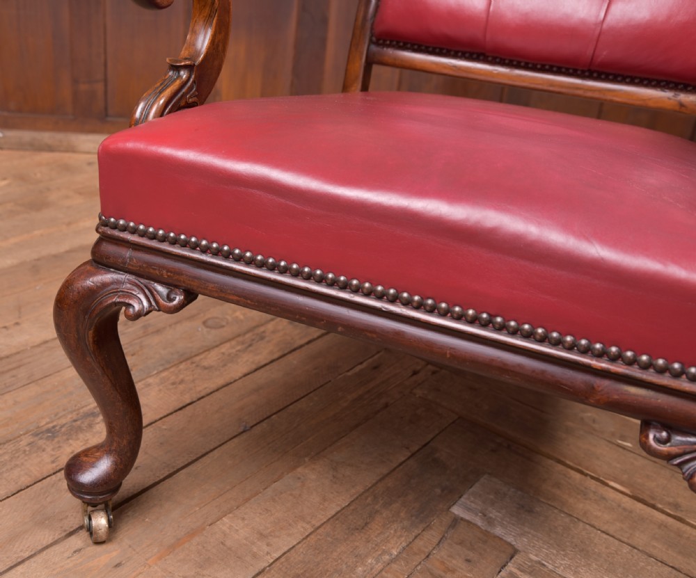 A Regency period rosewood armchair featuring dark red button-tufted leather upholstery, scrolled armrests, brass castors, and carved timber detailing. View IX