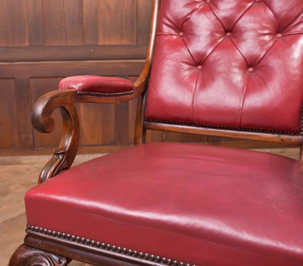 A Regency period rosewood armchair featuring dark red button-tufted leather upholstery, scrolled armrests, brass castors, and carved timber detailing. View X