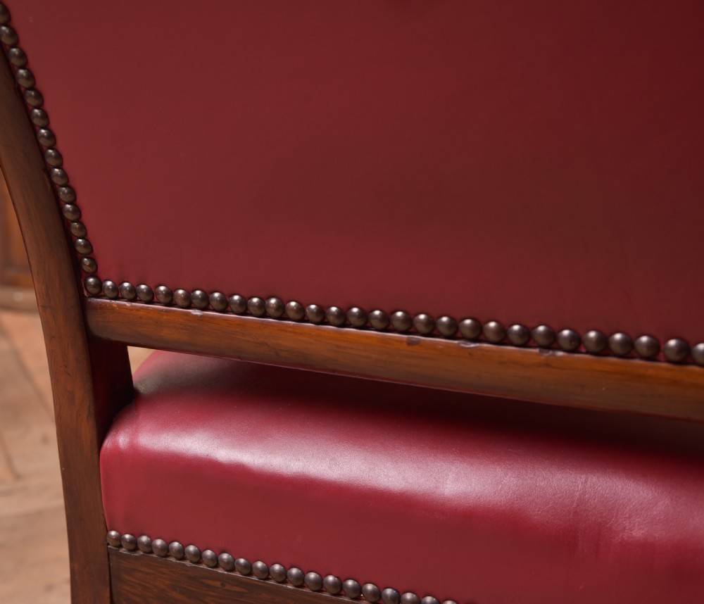 A Regency period rosewood armchair featuring dark red button-tufted leather upholstery, scrolled armrests, brass castors, and carved timber detailing. View XVI