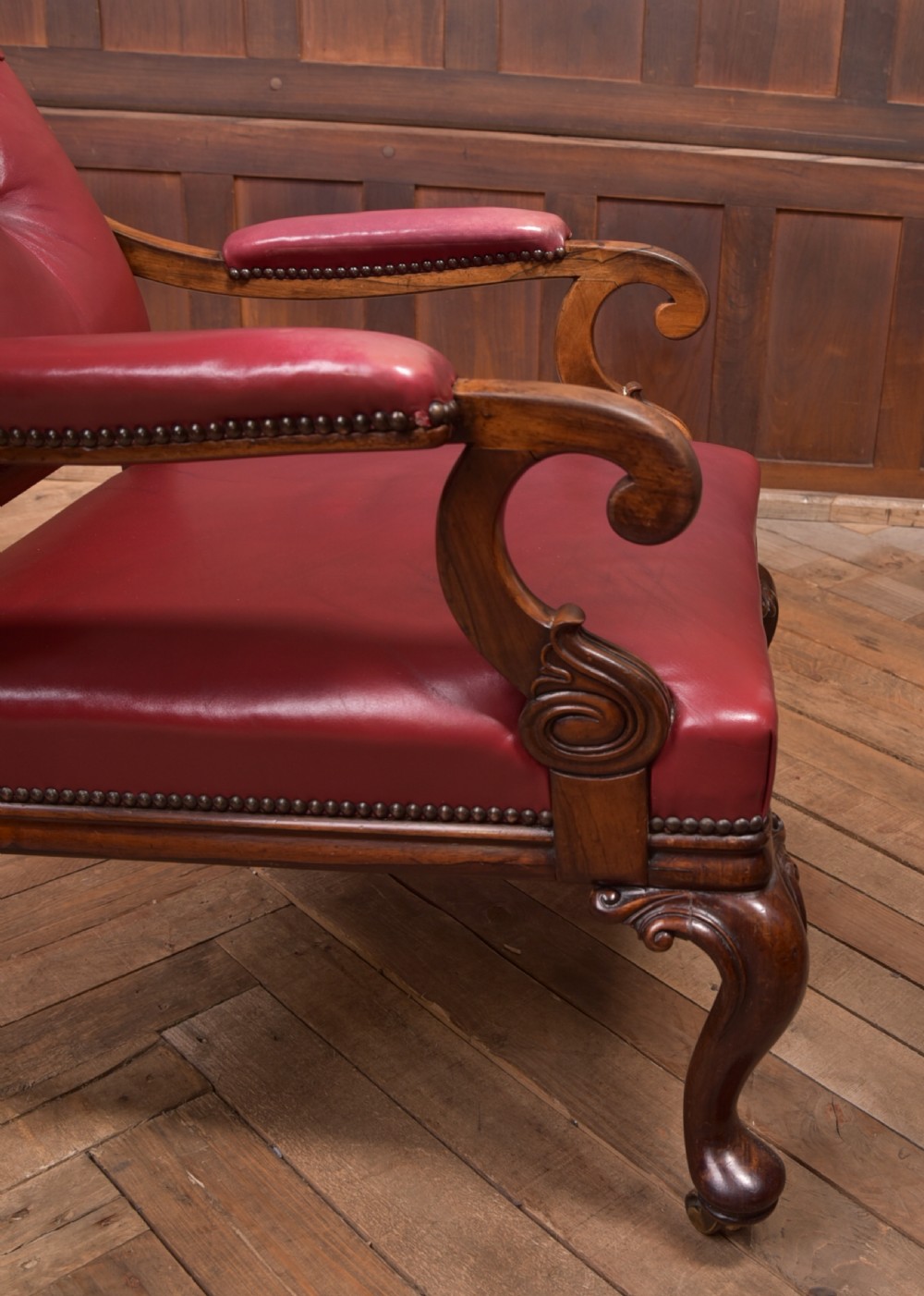 A Regency period rosewood armchair featuring dark red button-tufted leather upholstery, scrolled armrests, brass castors, and carved timber detailing. View XVIII