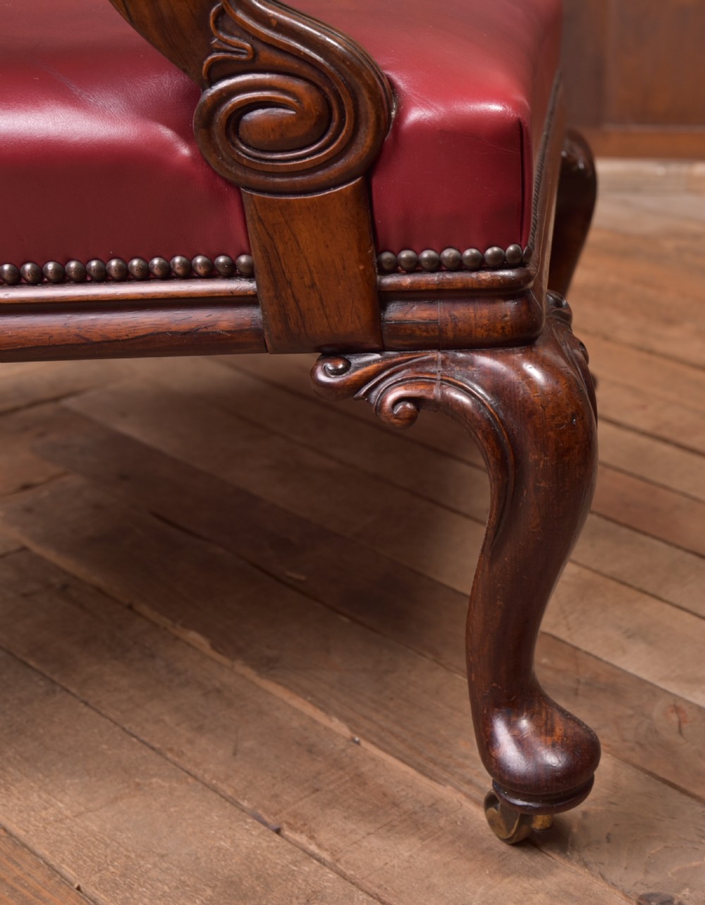 A Regency period rosewood armchair featuring dark red button-tufted leather upholstery, scrolled armrests, brass castors, and carved timber detailing. View XXIV